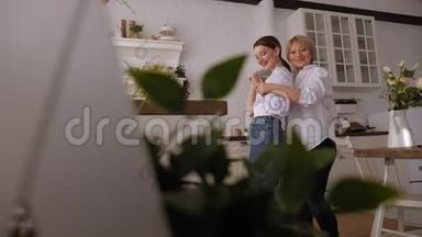 一位年迈的母亲和一个成年的女儿在厨房里跳舞，在家里玩得开心